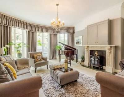 Sitting room with a baby grand piano and chandelier at Llwynhelig House, Vale of Glamorgan