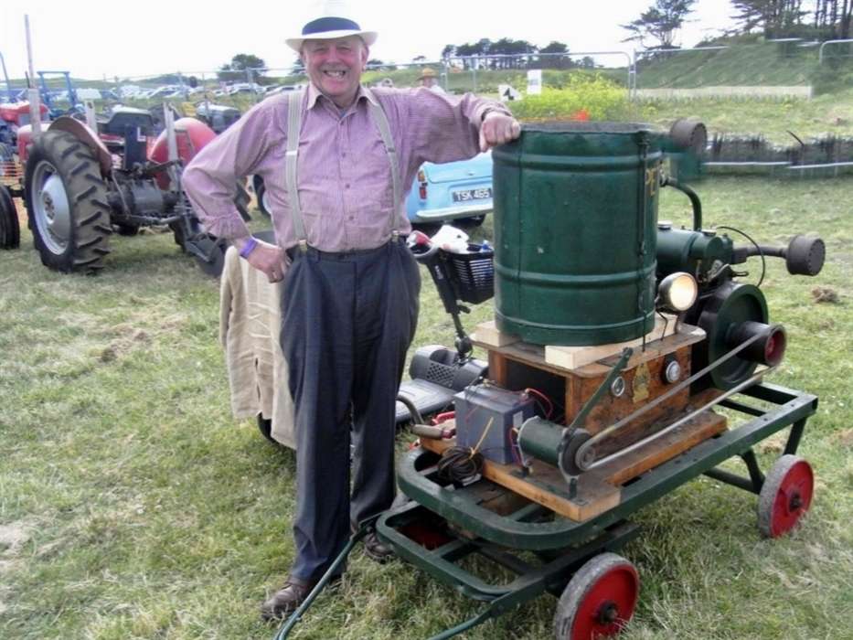 Proud exhibitor standing next to a green stationary engine at the Tywi Valley Vintage Show with a classic tractor behind him