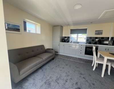 Living area of a chalet at The Bay Caravan Park with a sofa, kitchen units and a dining table by the window