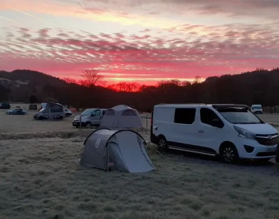 Tents and a campervan on the field at Dolgam Campsite under a red dawn sky
