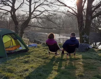 Two campers sitting in chairs beside a green tent looking out over the river at Dolgam