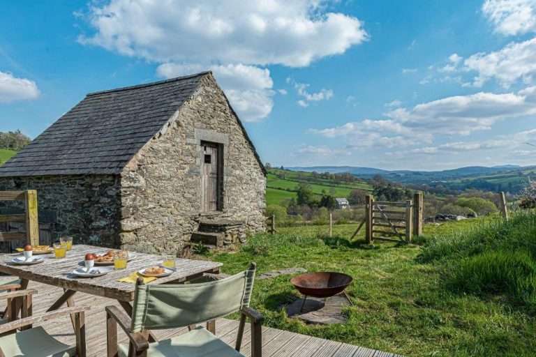 Stone barn with a slate roof standing above a gate and green fields near Betws-y-Coed