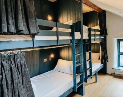 Bunk beds with privacy curtains and dark panelling in a dormitory at Base Camp Snowdonia