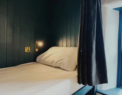 Single bunk at Base Camp Snowdonia with its privacy curtain drawn back and a reading light on